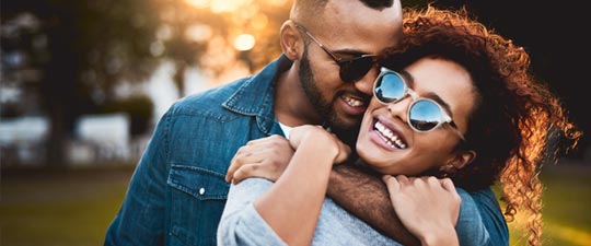 young couple with sunglasses hugging outside