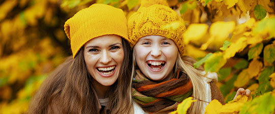 Mother and daughter wearing fall colors and smiling among the fall leaves