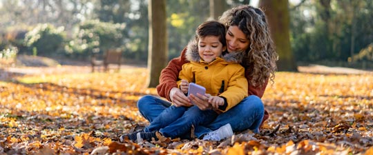 young mother with son looking at phone while sitting on leaves