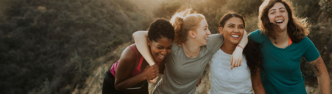 Female friends laughing as they hike, arms around each other.